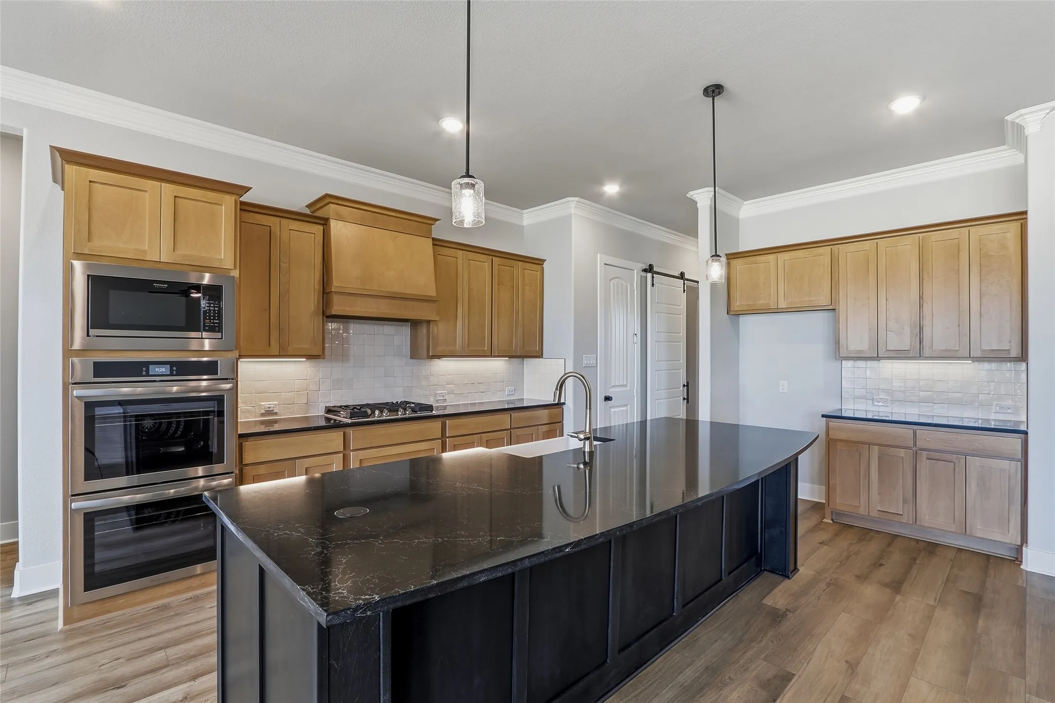 Kitchen featuring ornamental molding, dark stone counters, hanging light fixtures, light wood finished floors, and stainless steel appliances