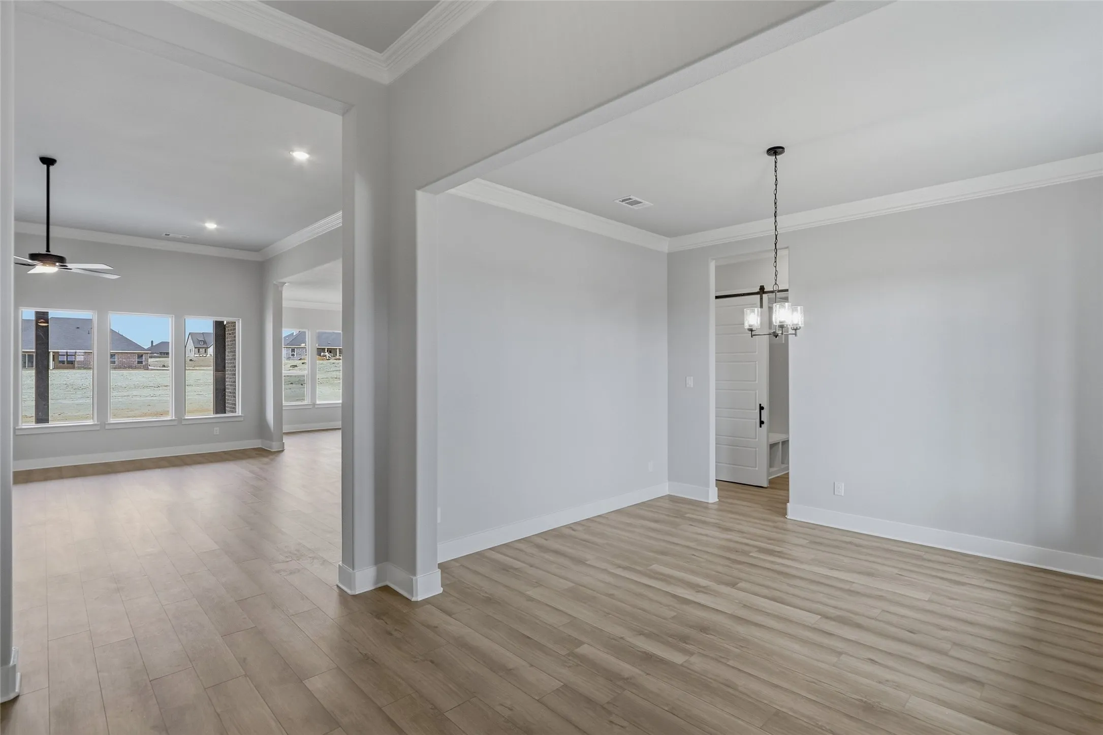 Unfurnished dining area featuring crown molding, light wood finished floors, ceiling fan, and suspended lighting