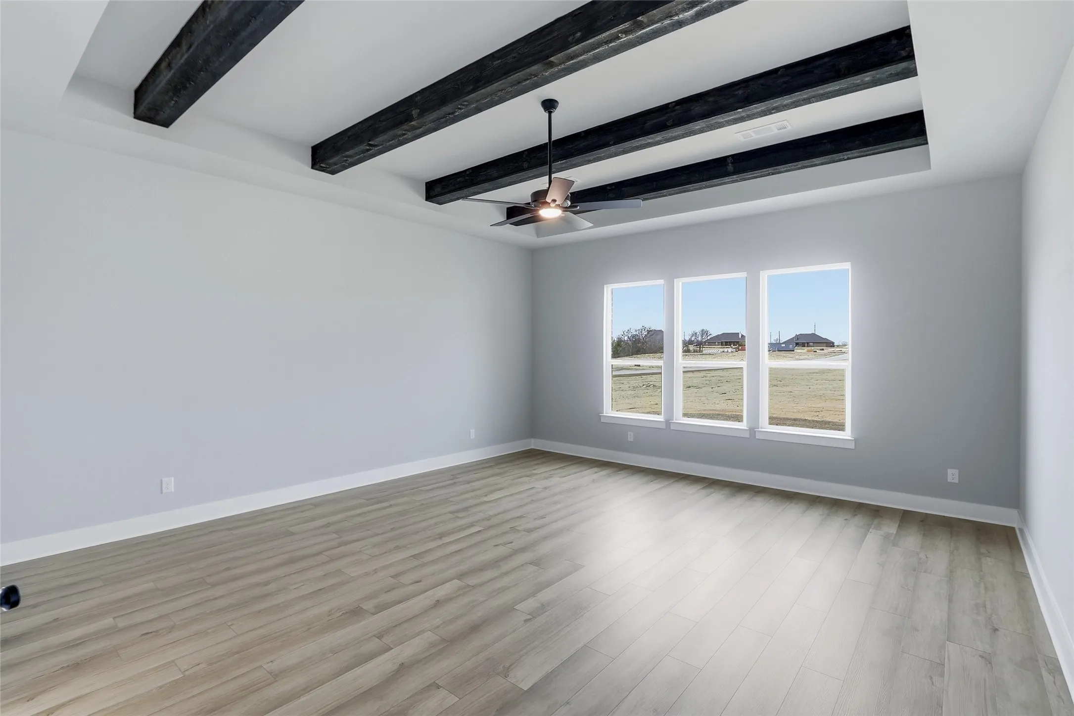 Empty room with beam ceiling, a ceiling fan, and light wood finished floors