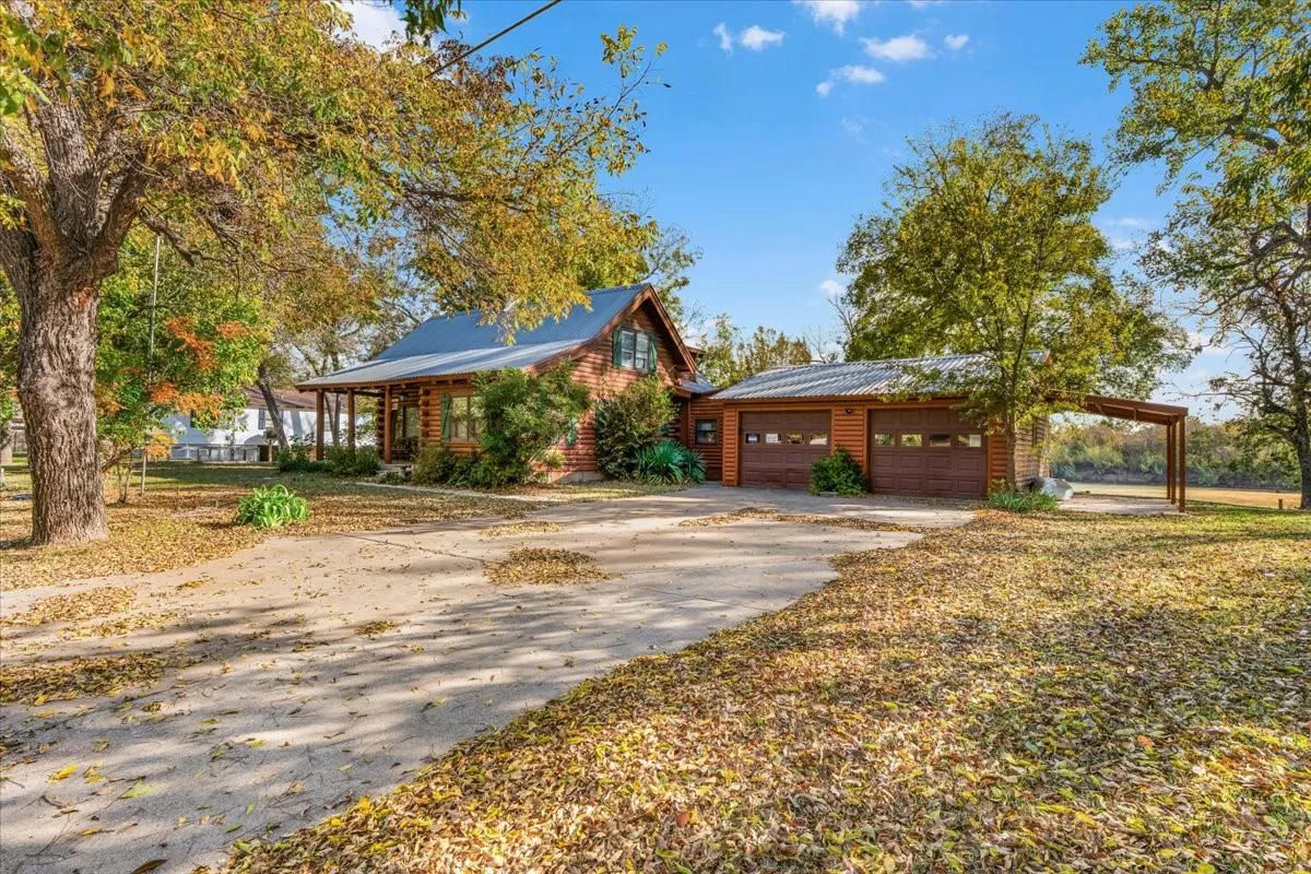 View of front of house featuring a garage, log veneer siding, asphalt driveway, and a carport