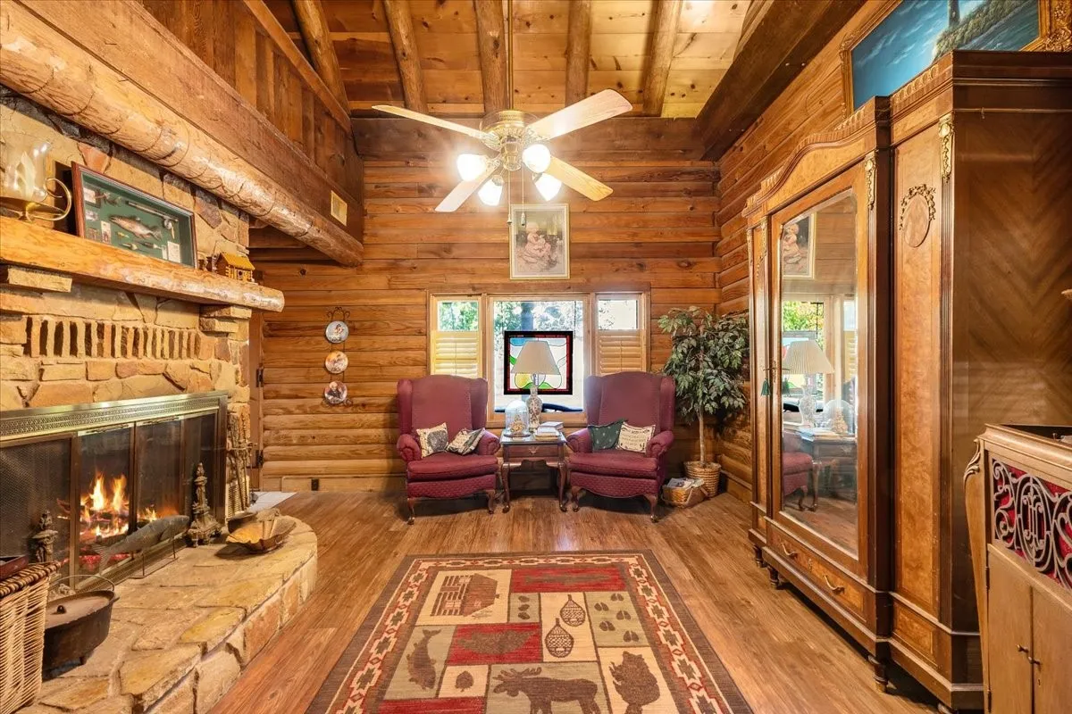 Sitting room with wood finished floors, high vaulted ceiling, a wood ceiling with exposed beams, a stone fireplace, and a ceiling fan