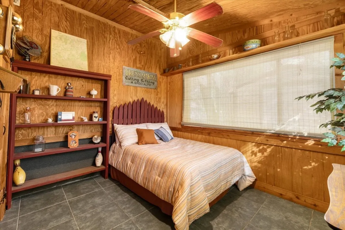 Bedroom featuring wood walls, dark tile patterned floors, wood ceiling, and a ceiling fan