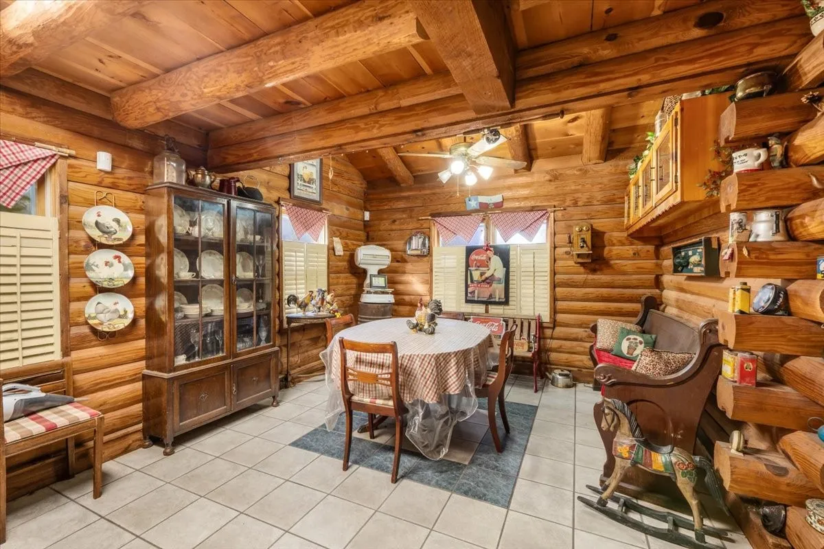 Dining space with a wood ceiling with exposed beams, light tile patterned floors, log walls, and ceiling fan