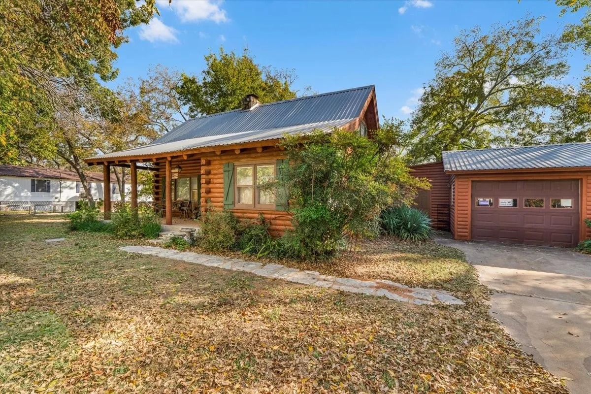 Cabin featuring a metal roof, concrete driveway, covered porch, a chimney, and log siding