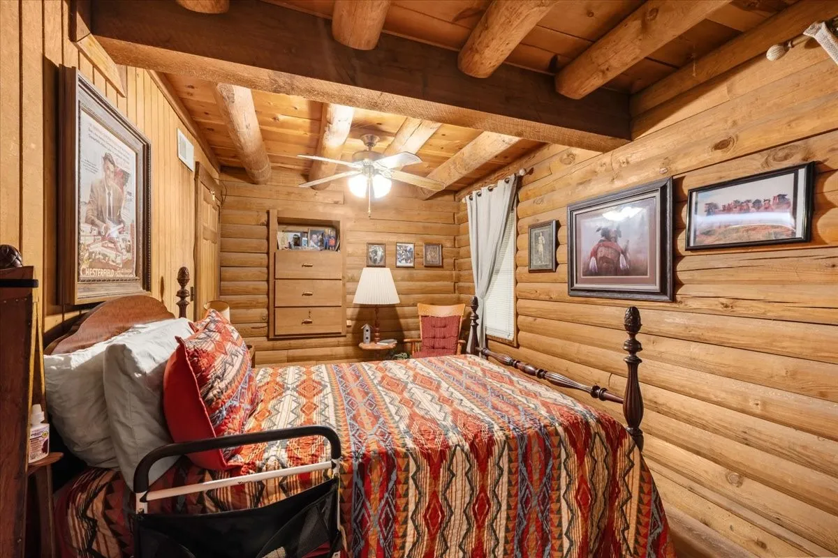 Bedroom with a wood ceiling with exposed beams, rustic walls, and a ceiling fan