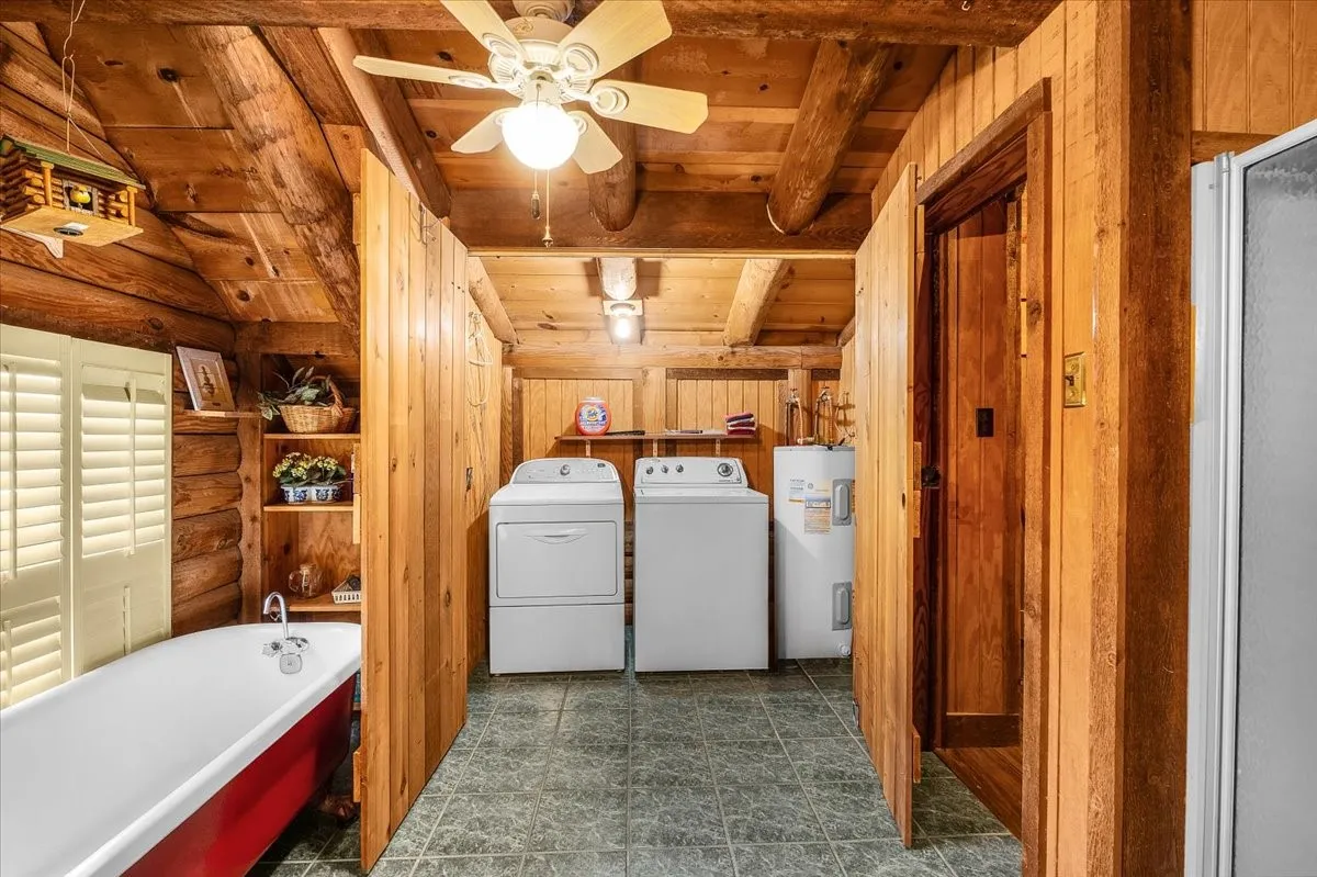 Washroom featuring a wood ceiling with exposed beams, electric water heater, separate washer and dryer, ceiling fan, and wood walls