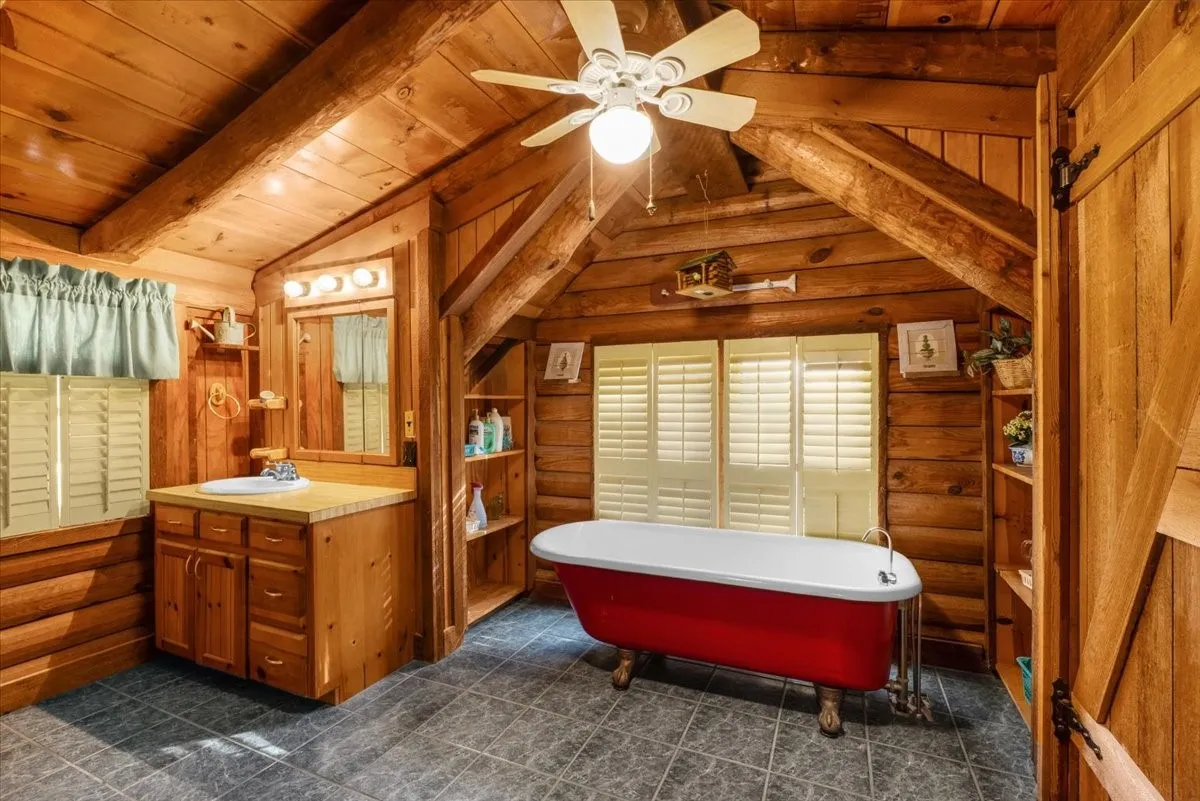 Bathroom featuring log walls, a freestanding bath, vanity, ceiling fan, and wood ceiling