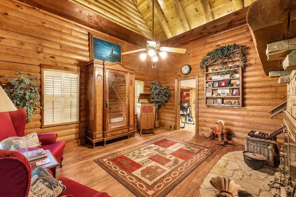 Living area with log walls, high vaulted ceiling, wood finished floors, a wooden ceiling with exposed beams, and a ceiling fan