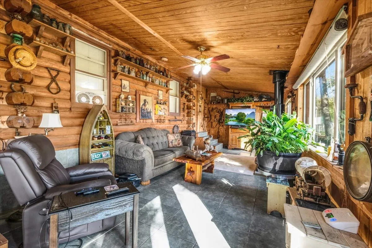 Living area with a wood stove, wooden ceiling, tile patterned flooring, and ceiling fan