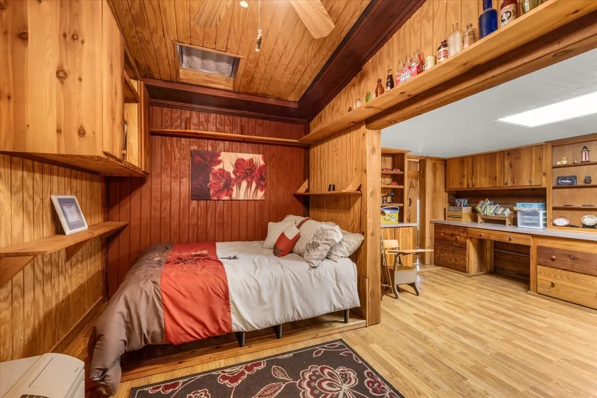 Bedroom featuring light wood-type flooring, built in desk, wood walls, and wooden ceiling