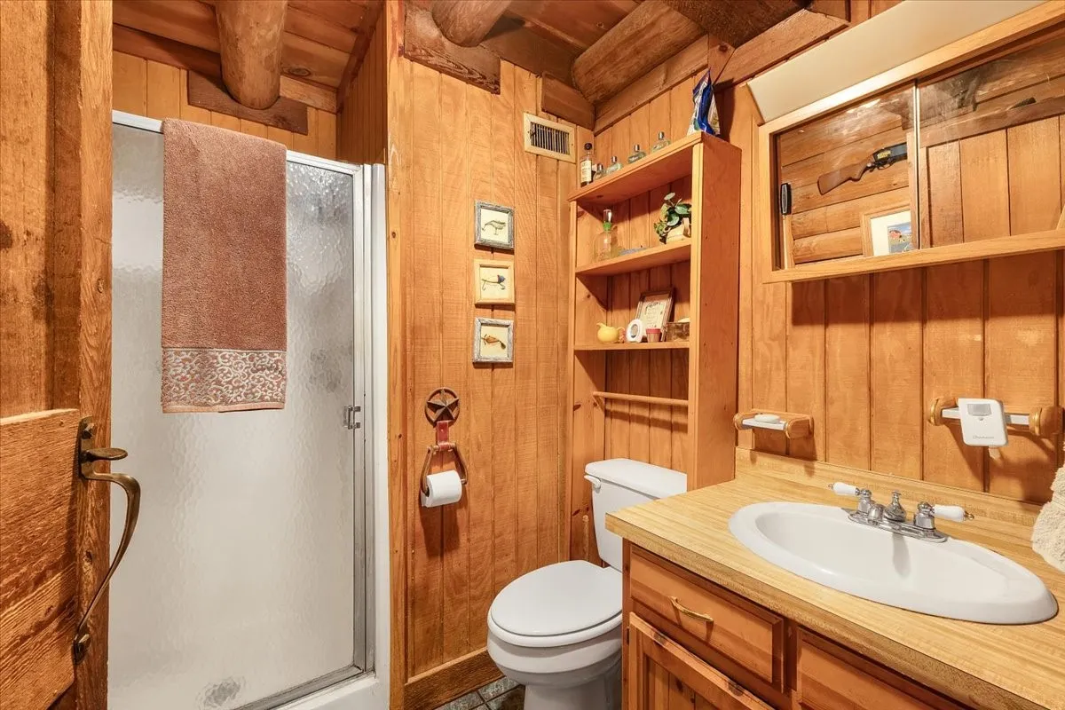 Full bathroom with wood walls, a stall shower, vanity, and a wooden ceiling with exposed beams