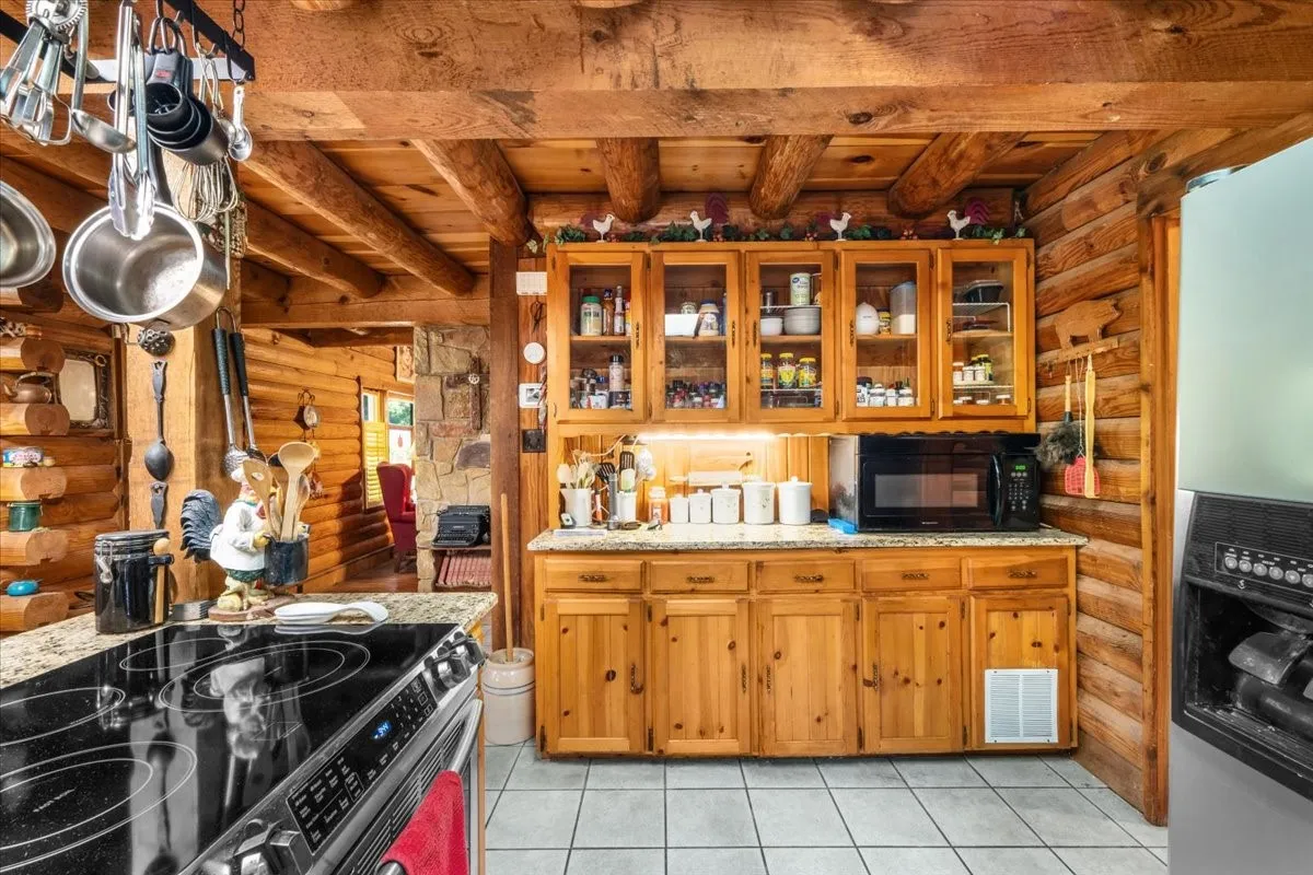 Kitchen featuring glass insert cabinets, rustic walls, electric range, light tile patterned floors, and stainless steel fridge with ice dispenser