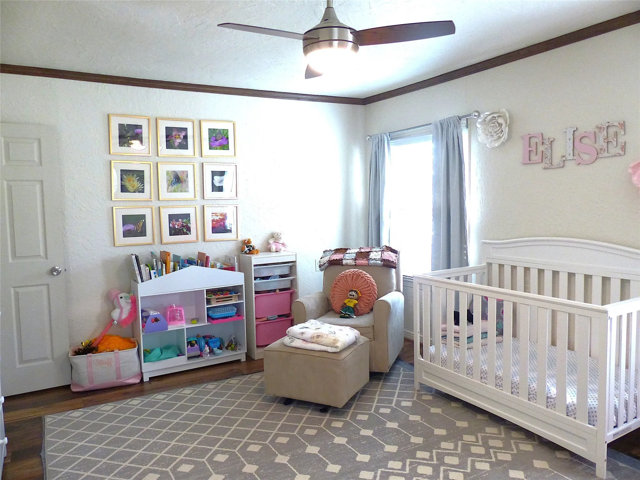 Bedroom with a crib, crown molding, dark wood-style floors, a ceiling fan, and a textured wall