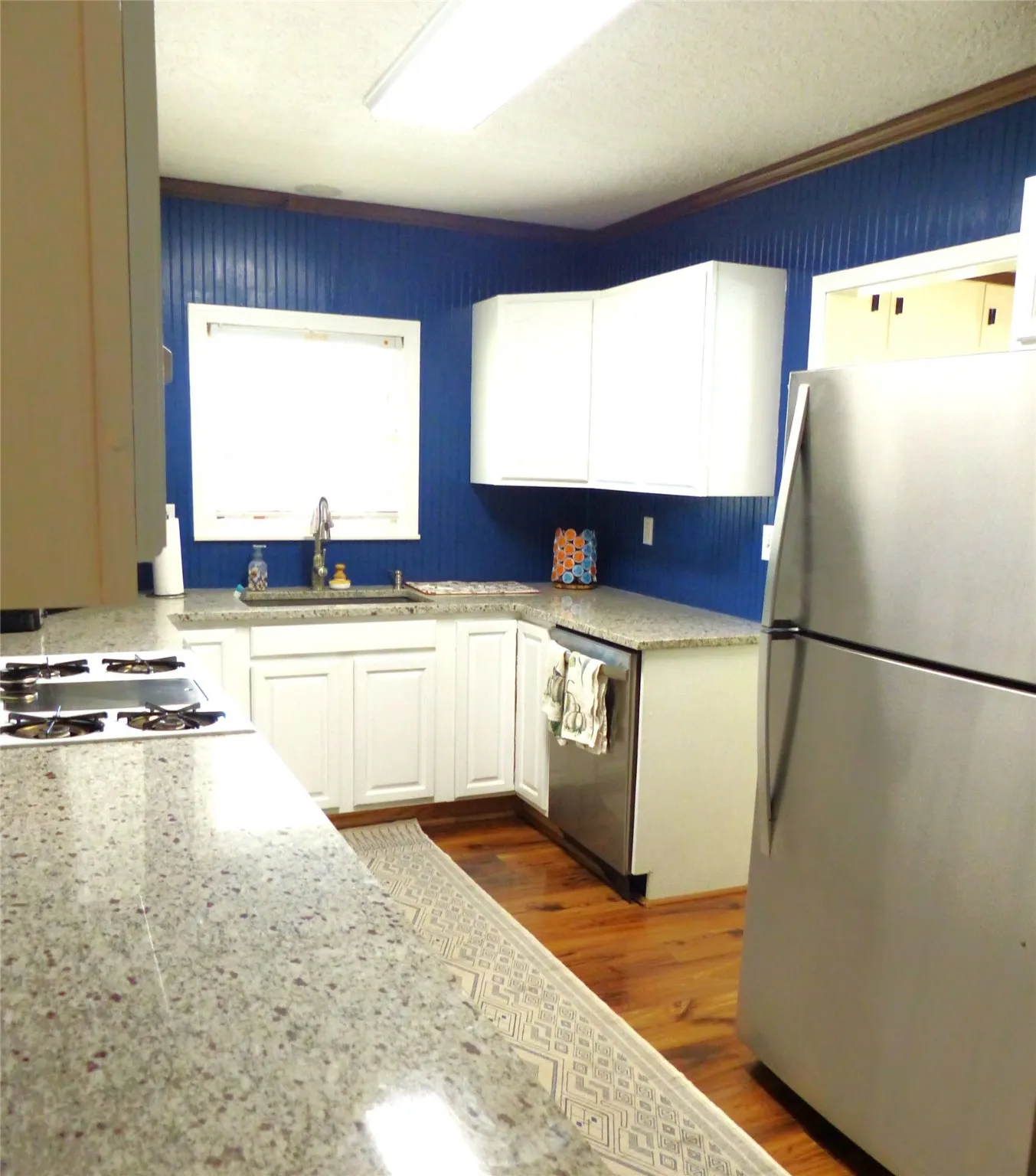 Kitchen with white cabinetry, appliances with stainless steel finishes, dark wood-style flooring, and light stone counters