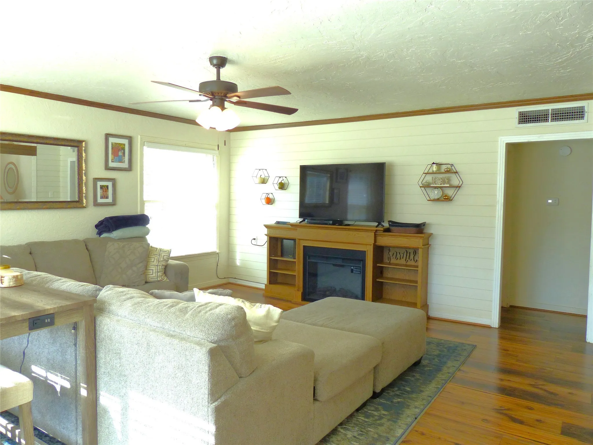 Living room featuring crown molding, wood finished floors, a glass covered fireplace, ceiling fan, and a textured ceiling