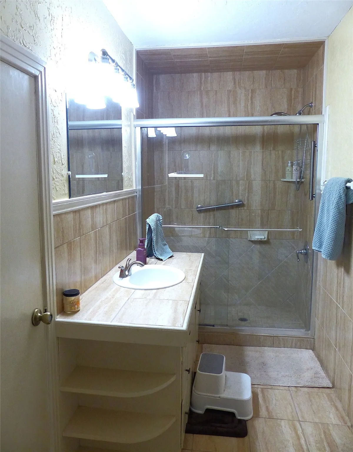 Bathroom featuring vanity, light tile patterned floors, a stall shower, and a textured wall