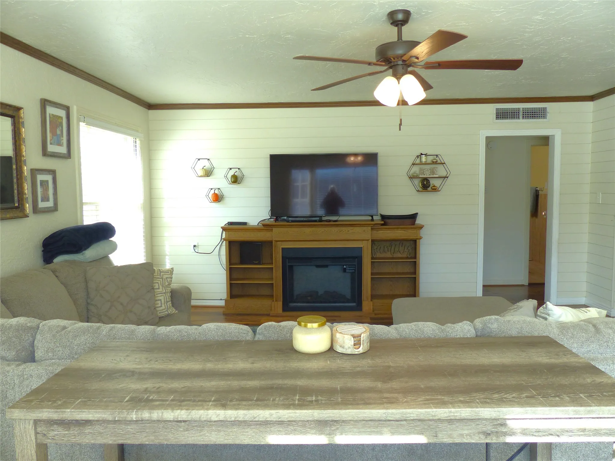 Living area featuring crown molding, a glass covered fireplace, a textured ceiling, wooden walls, and ceiling fan