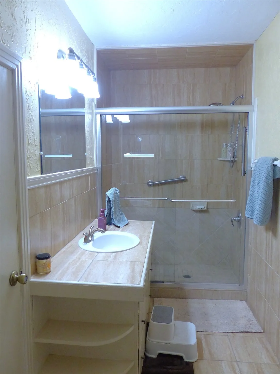 Full bathroom with vanity, a textured wall, a shower stall, and tile walls