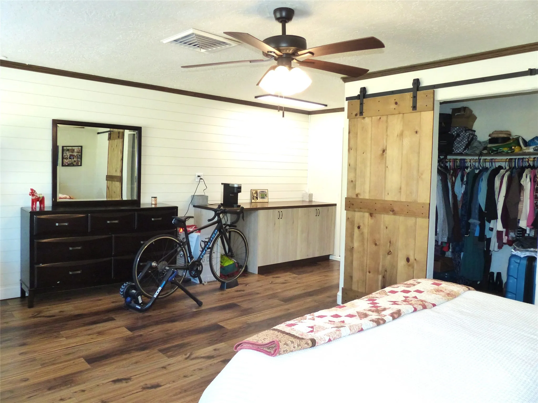 Bedroom featuring crown molding, a textured ceiling, a barn door, dark wood-type flooring, and a closet