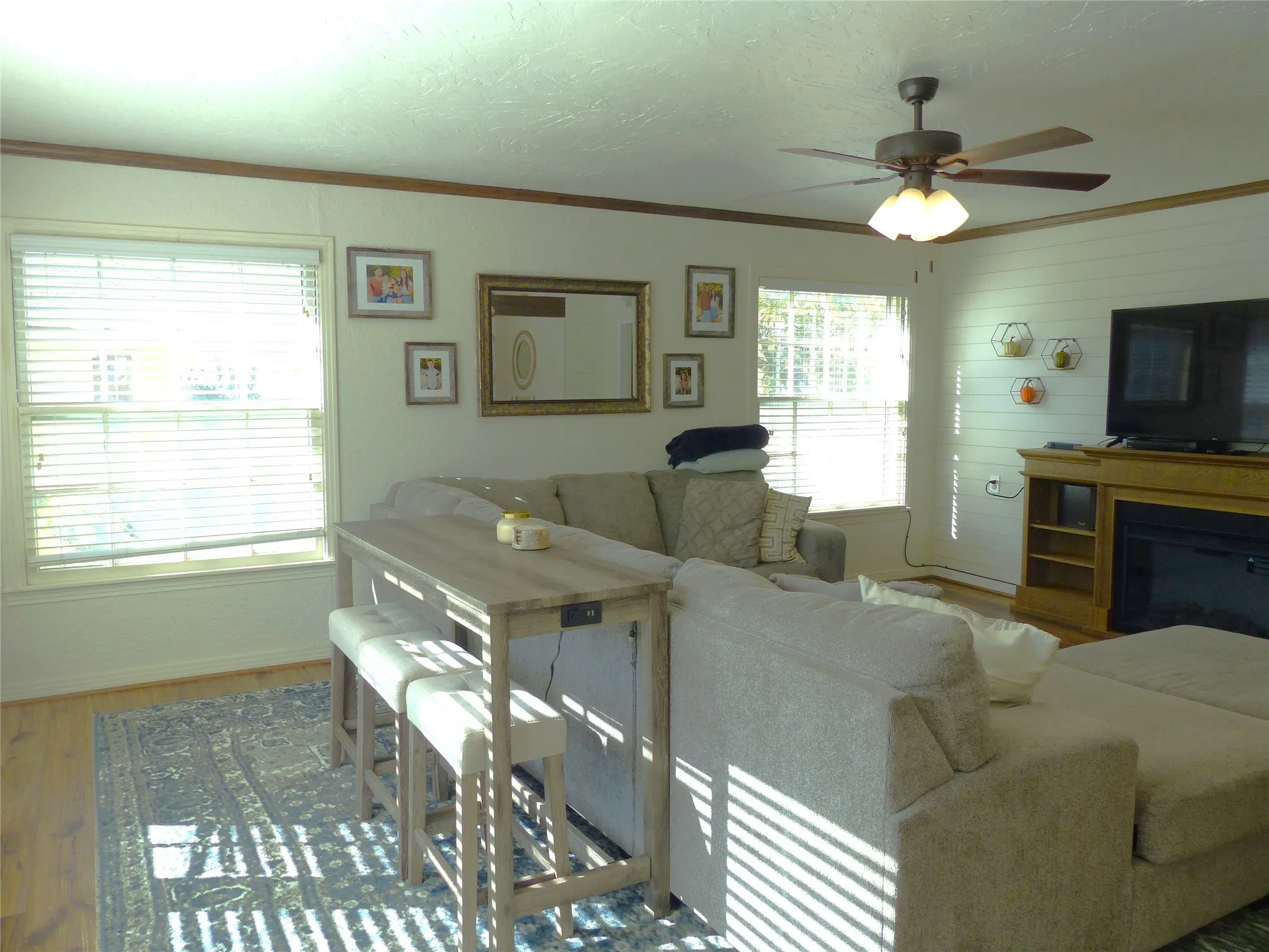Living area with ornamental molding, wood finished floors, a textured ceiling, a glass covered fireplace, and a ceiling fan