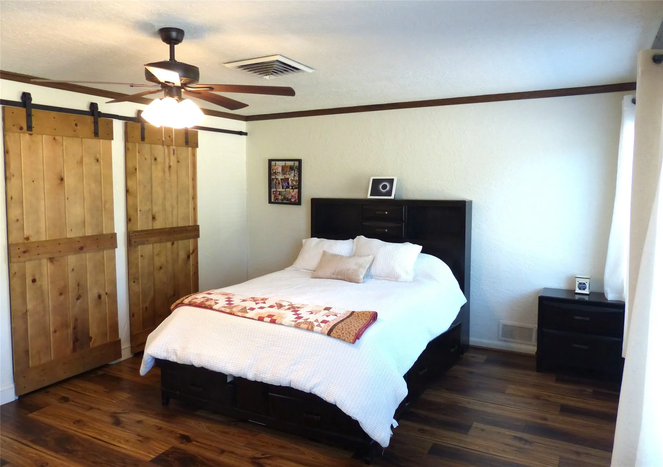 Bedroom featuring crown molding, dark wood finished floors, a barn door, a ceiling fan, and a textured wall