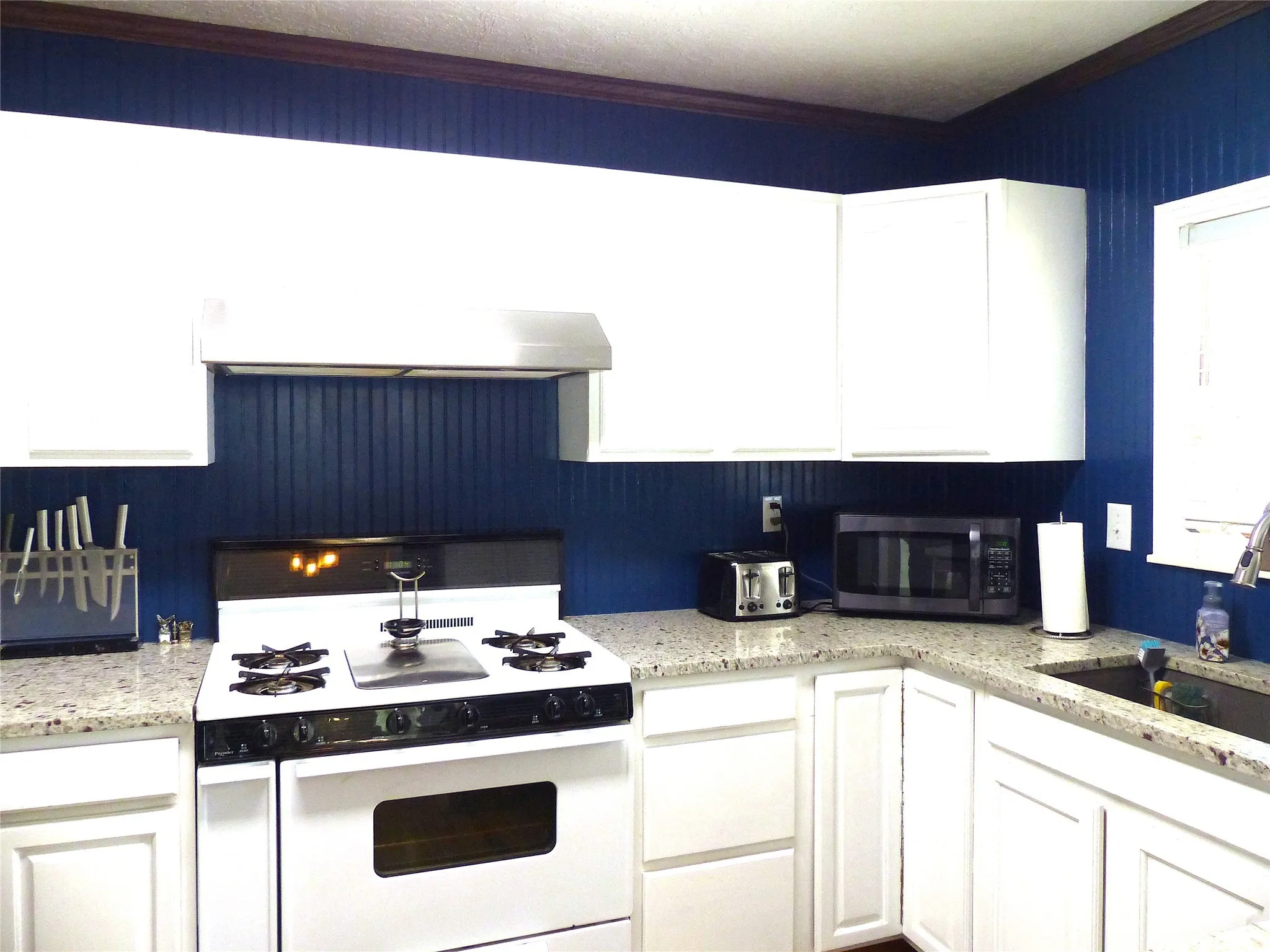 Kitchen with white gas range, white cabinets, stainless steel microwave, and extractor fan