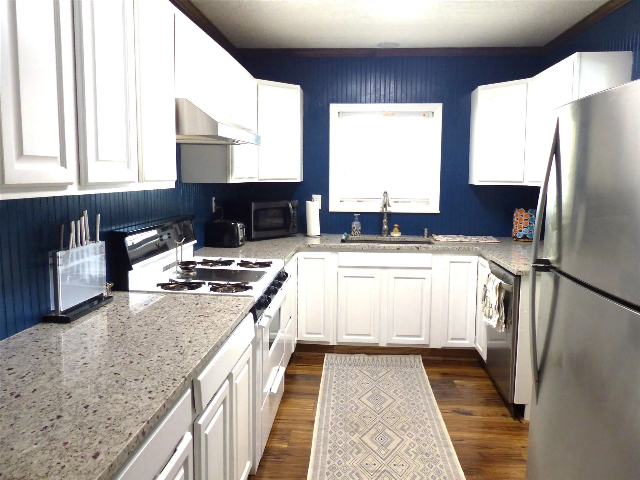 Kitchen featuring stainless steel appliances, white cabinets, dark wood-type flooring, and light stone countertops