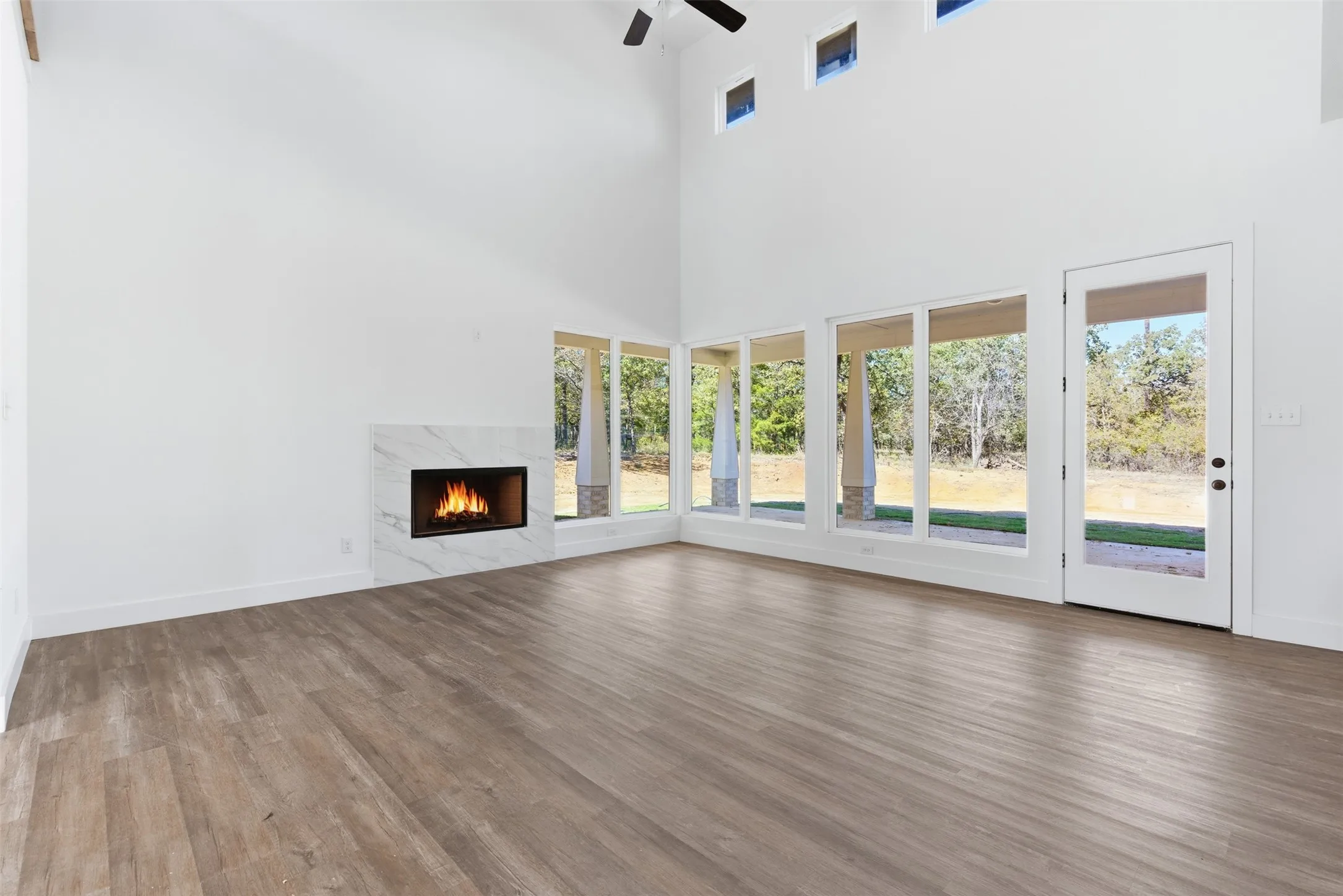Unfurnished living room featuring a fireplace, a high ceiling, wood finished floors, and ceiling fan