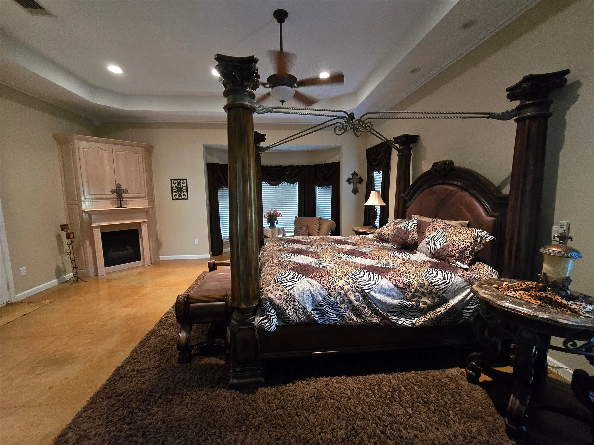 Bedroom with a tray ceiling, a fireplace, light carpet, recessed lighting, and a ceiling fan