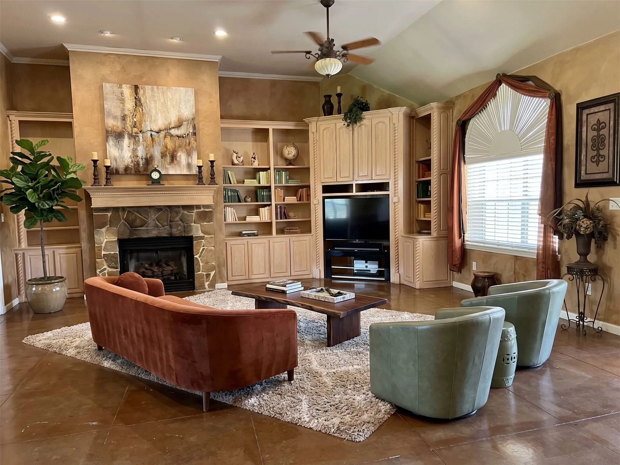 Stained concrete flooring, a stone-faced fireplace with a mantel, built-in shelving, vaulted ceilings, and an arched window