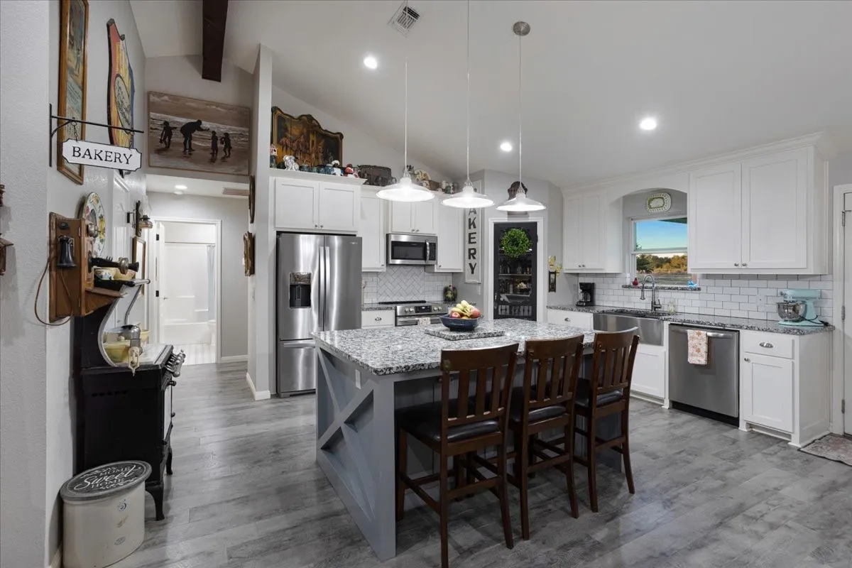 Kitchen featuring light stone countertops, decorative light fixtures, appliances with stainless steel finishes, a kitchen island, and tasteful backsplash