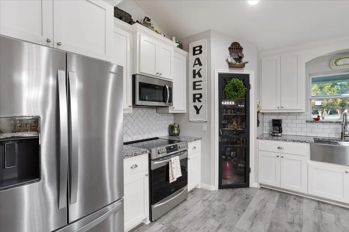 Kitchen with stainless steel appliances, light stone countertops, white cabinets, and light wood-type flooring