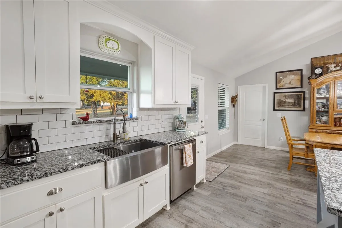 Kitchen featuring white cabinetry, dark stone countertops, lofted ceiling, plenty of natural light, and light wood-style flooring