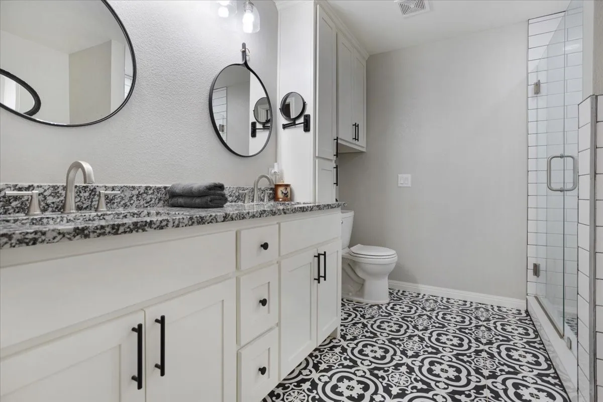 Full bath with double vanity, a stall shower, light tile patterned flooring, and a textured wall