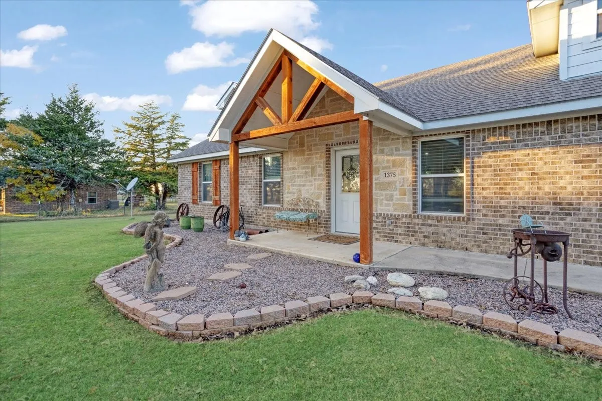 Back of property featuring covered porch, roof with shingles, and brick siding