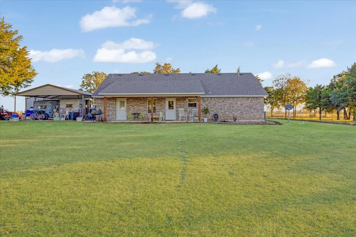 Rear view of property featuring a yard, a patio, brick siding, and roof with shingles