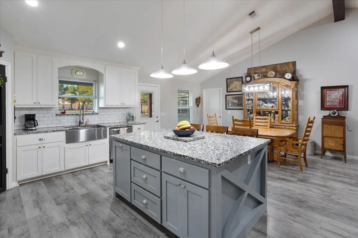 Kitchen featuring gray cabinetry, white cabinets, decorative light fixtures, light stone countertops, and a kitchen island