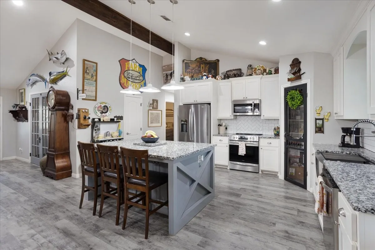 Kitchen featuring decorative backsplash, stainless steel appliances, hanging light fixtures, white cabinets, and beam ceiling