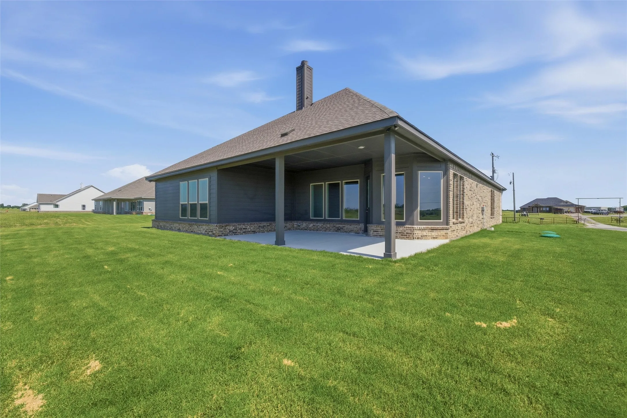 Expansive rear patio featuring a covered area with support columns, multiple windows, and a brick and siding exterior