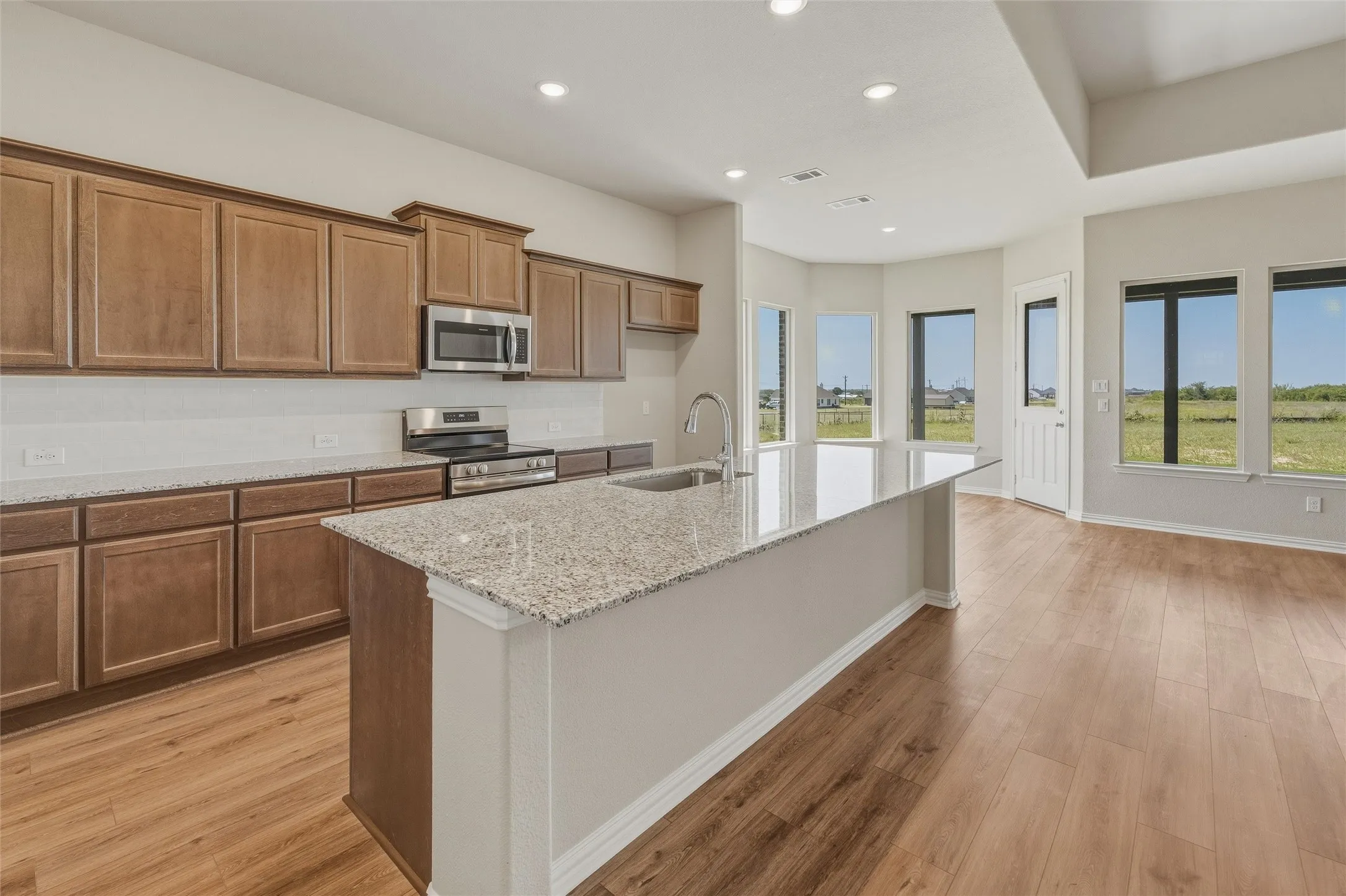 Open-concept kitchen featuring an island with a light-toned countertop, wood-finish flooring, and recessed lighting