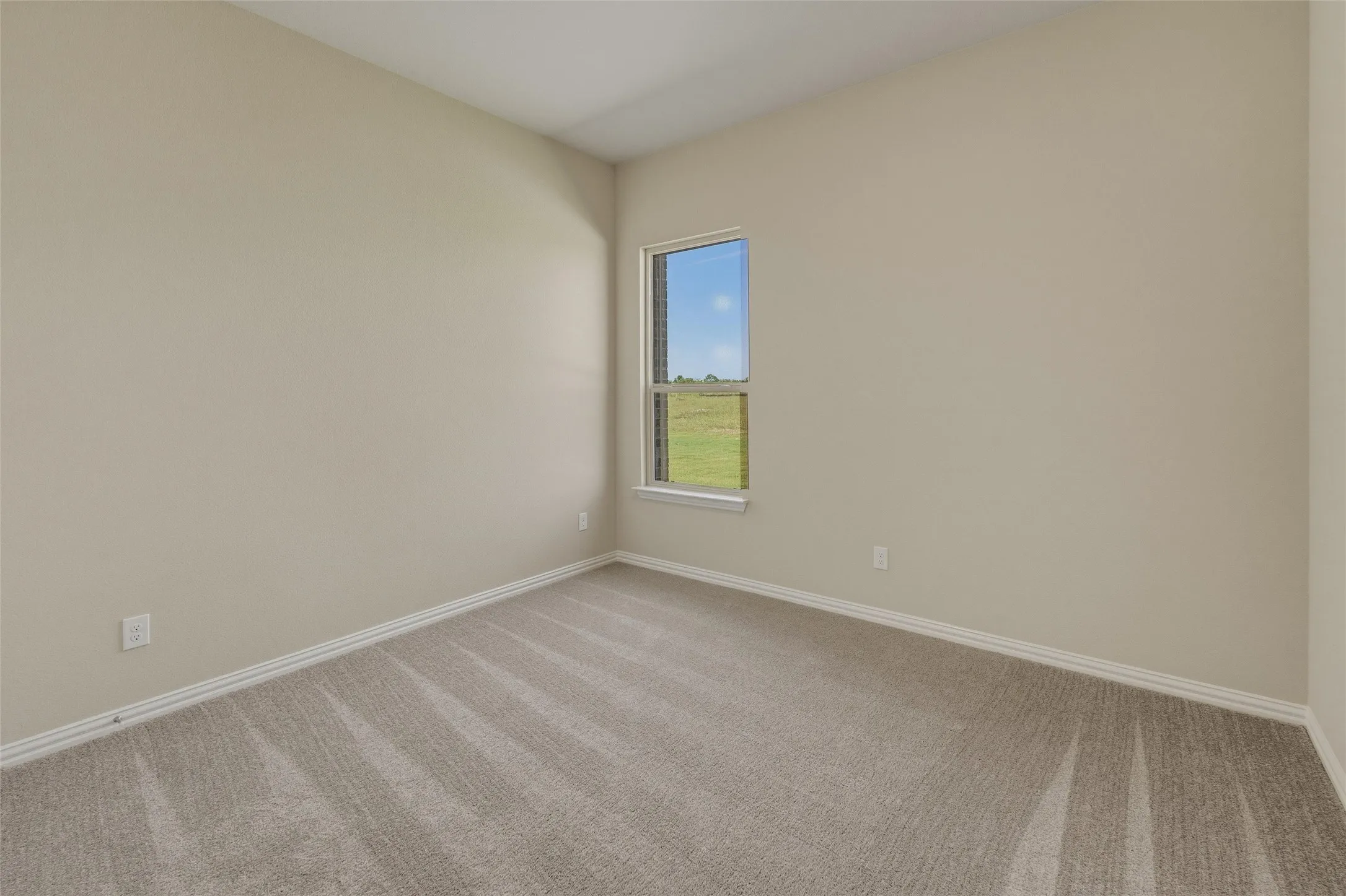 Carpeted interior room with neutral-toned walls, white baseboards, and a single window featuring a white frame
