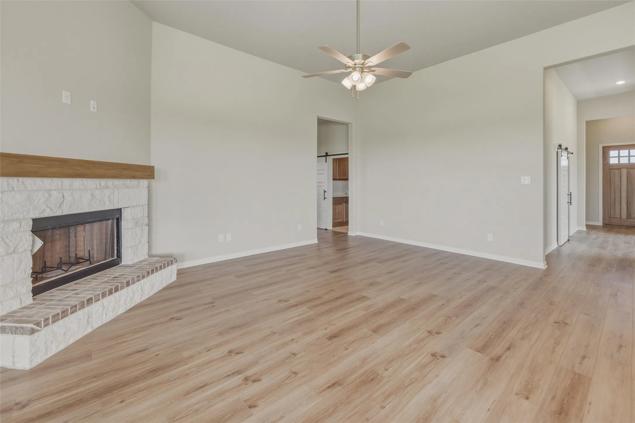 Spacious living area featuring wood-finish flooring, a stone fireplace with a brick hearth and wood mantel, and a ceiling fan