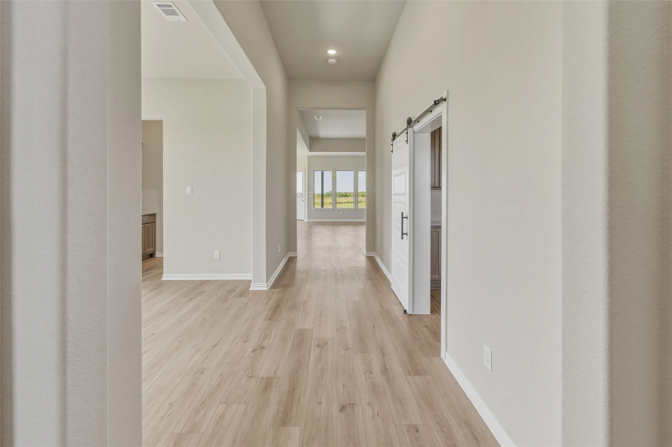 Expansive interior hallway with wood-finish flooring, recessed lighting, and a modern barn door