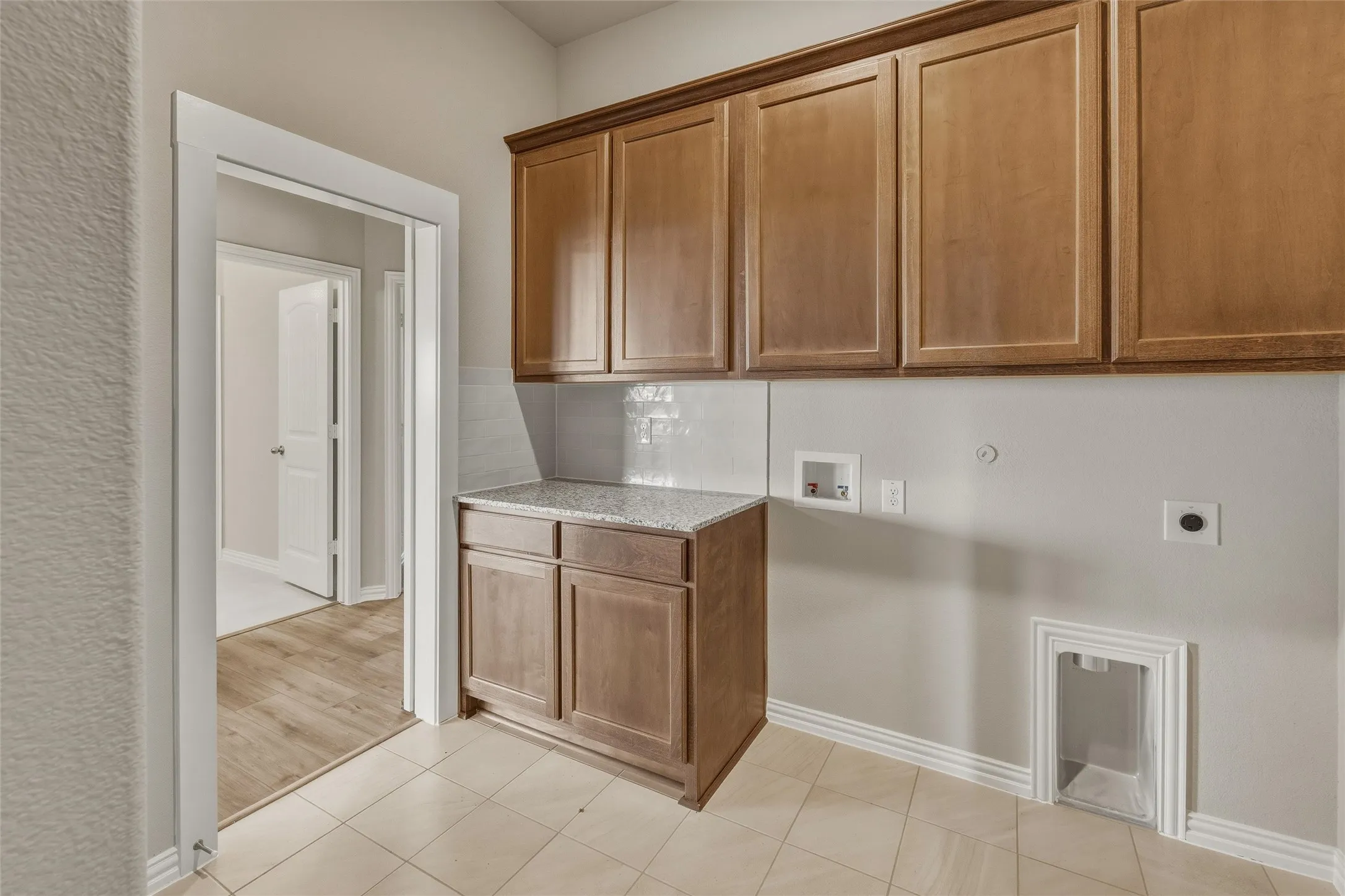 Utility room with light wood-finish cabinetry, a granite-finish countertop, and a tiled backsplash