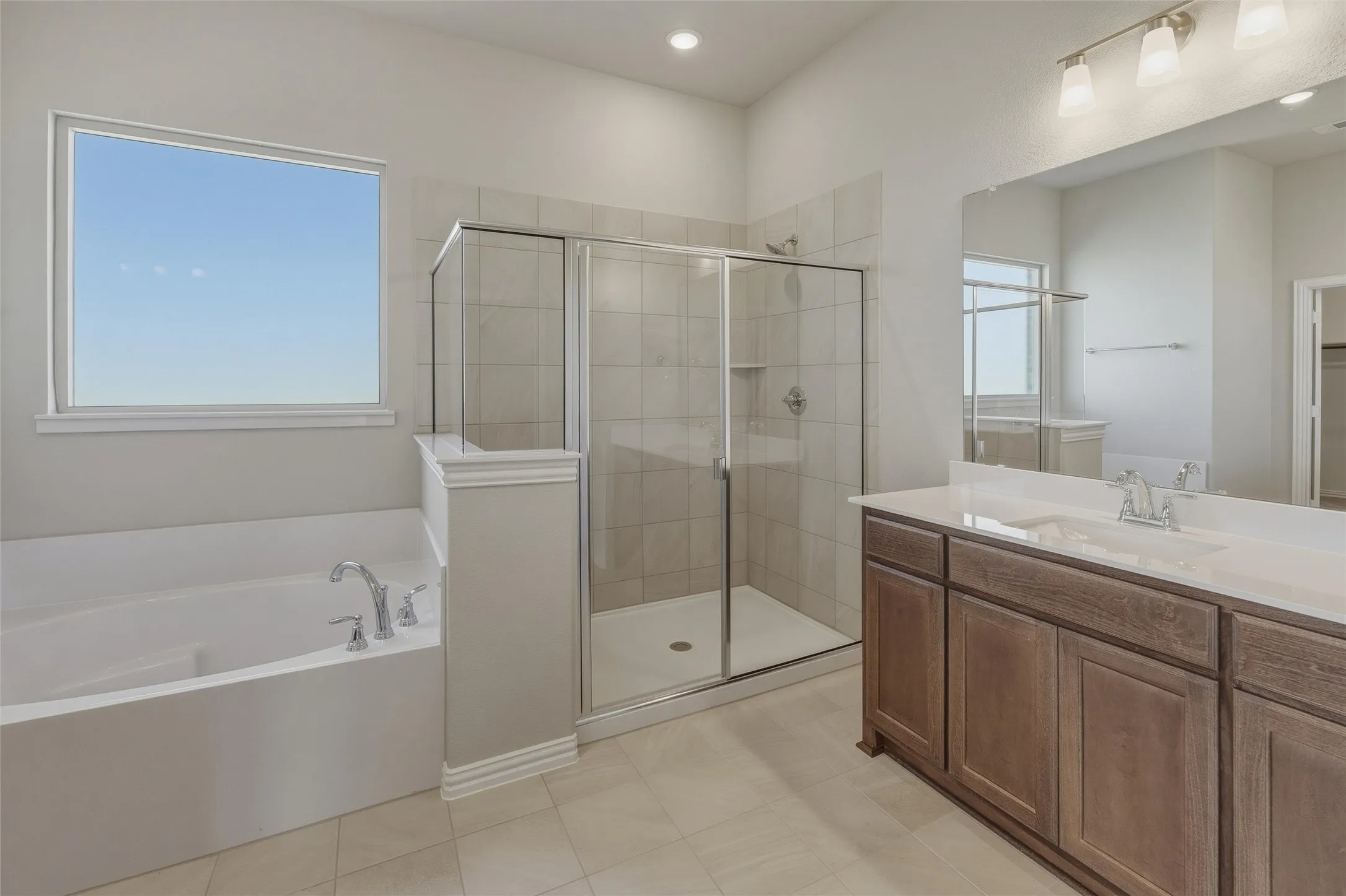 Bright bathroom featuring a large soaking tub, separate glass-enclosed shower, dual vanity with undermount sinks, and tile flooring