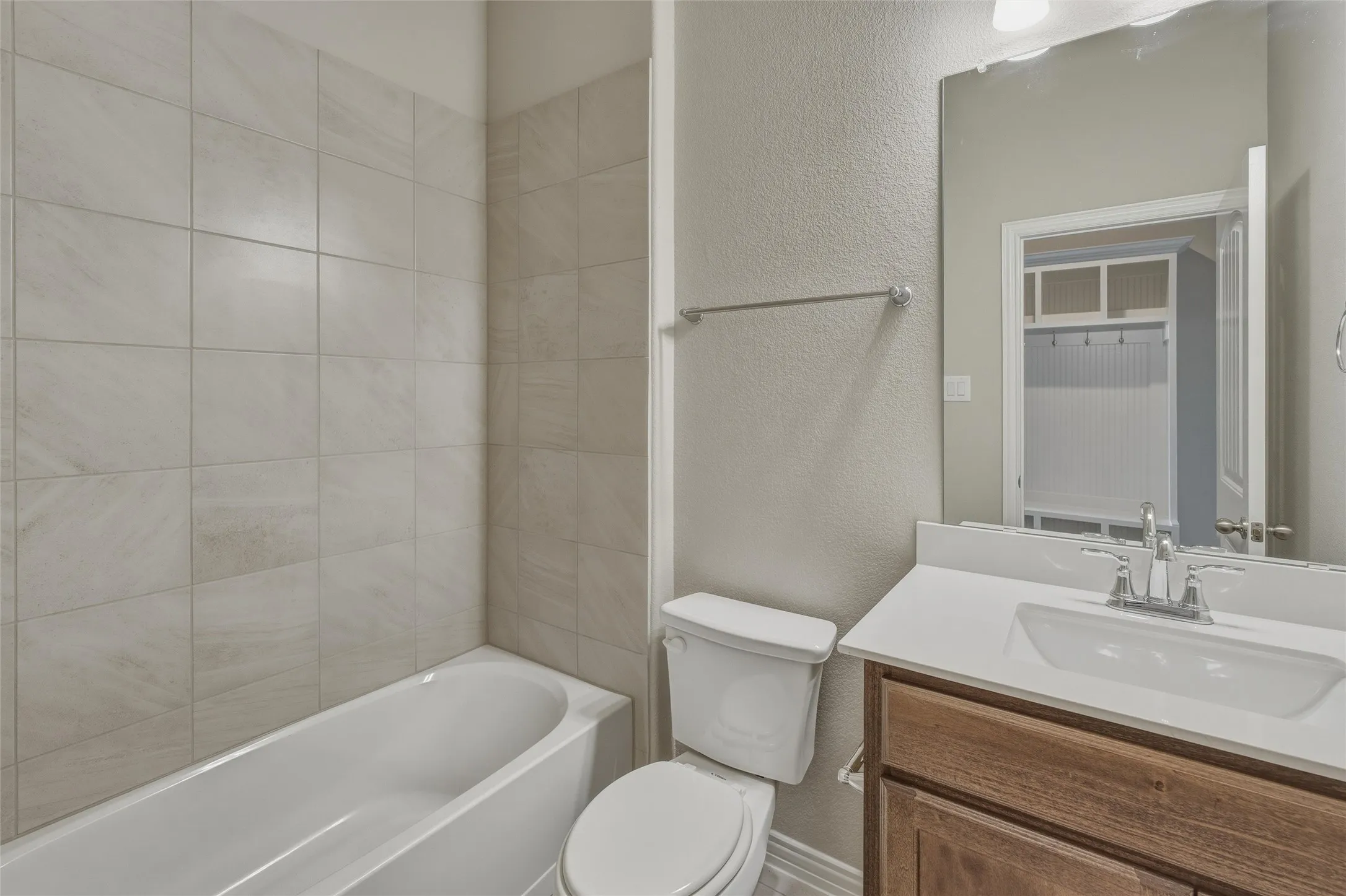 Bathroom featuring a white bathtub, ceramic tile surround, a wood-finish vanity with a white countertop and integrated sink, and a commode