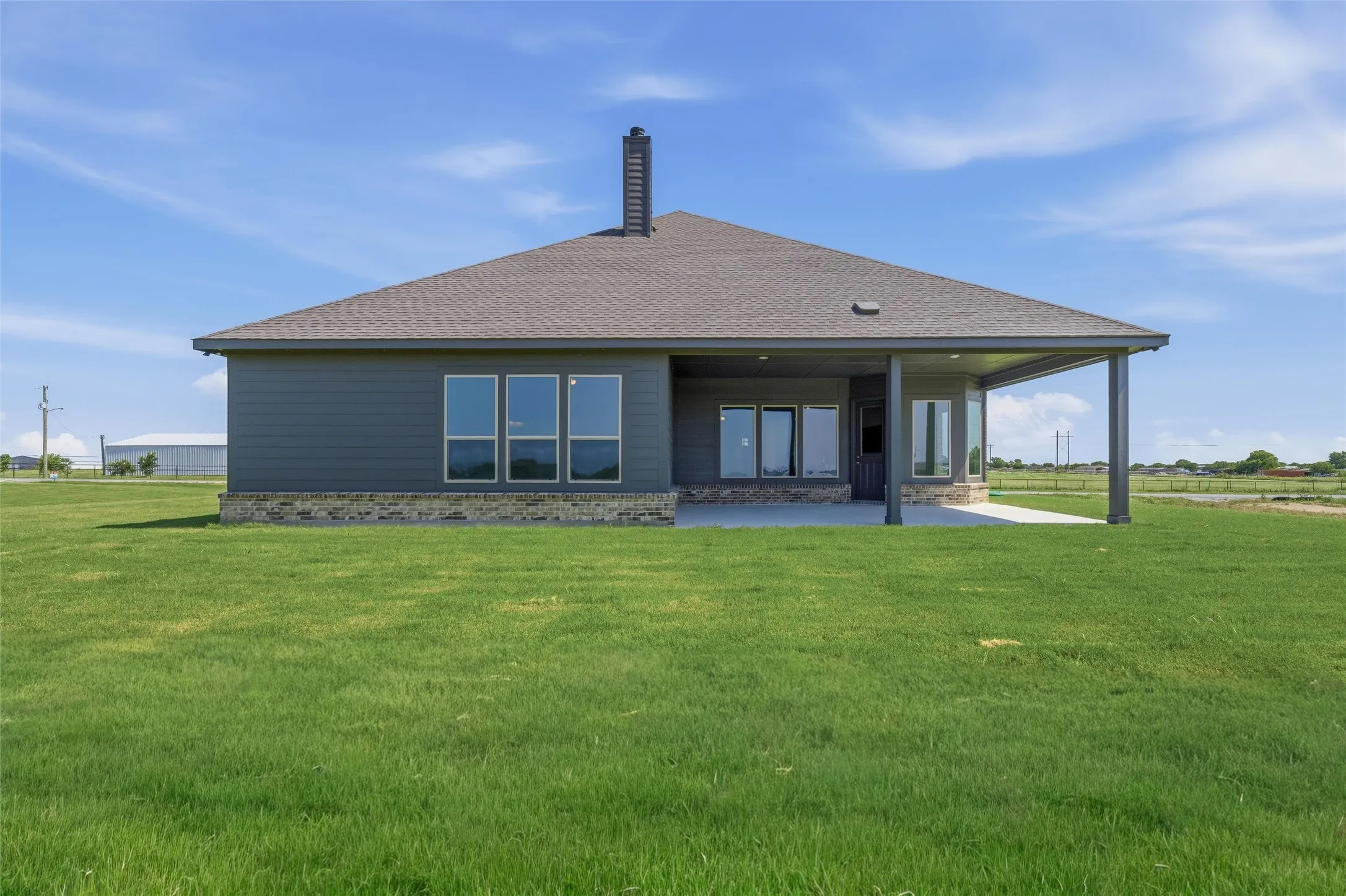 Rear exterior featuring a covered patio, extensive concrete slab, and a large grassy area