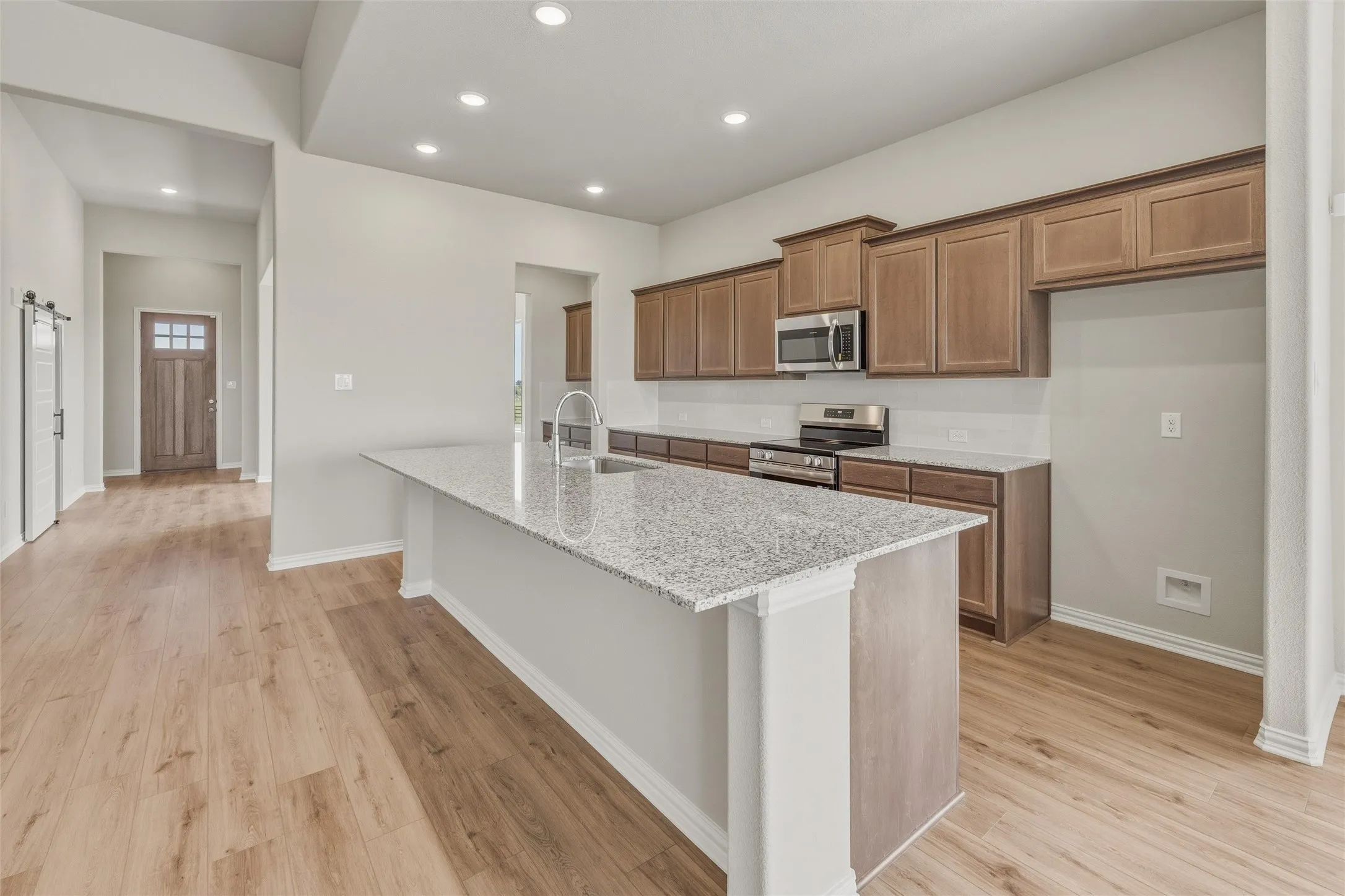 Open-concept kitchen featuring a large island with a light-colored countertop, wood-finish flooring, recessed lighting, wood cabinetry, and stainless steel appliances