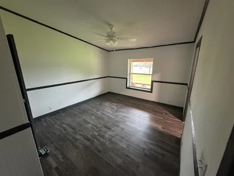 Empty room featuring dark wood finished floors, a textured ceiling, and a ceiling fan