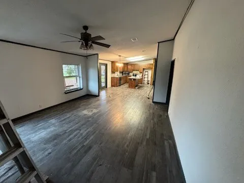 Unfurnished living room featuring dark wood-style flooring and a ceiling fan